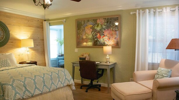 A bedroom with a bed, desk, chair, and a painting on the wall. - Winter Park charm. Close to Park Ave (Winter Park)