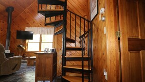 A wooden interior with a spiral staircase, a flat-screen TV, a small table, and a chair.