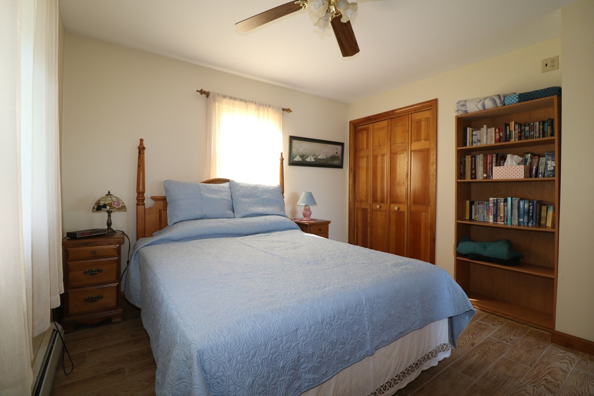 Une chambre à coucher comprenant un lit, une armoire en bois, une table de chevet, une lampe et une bibliothèque.