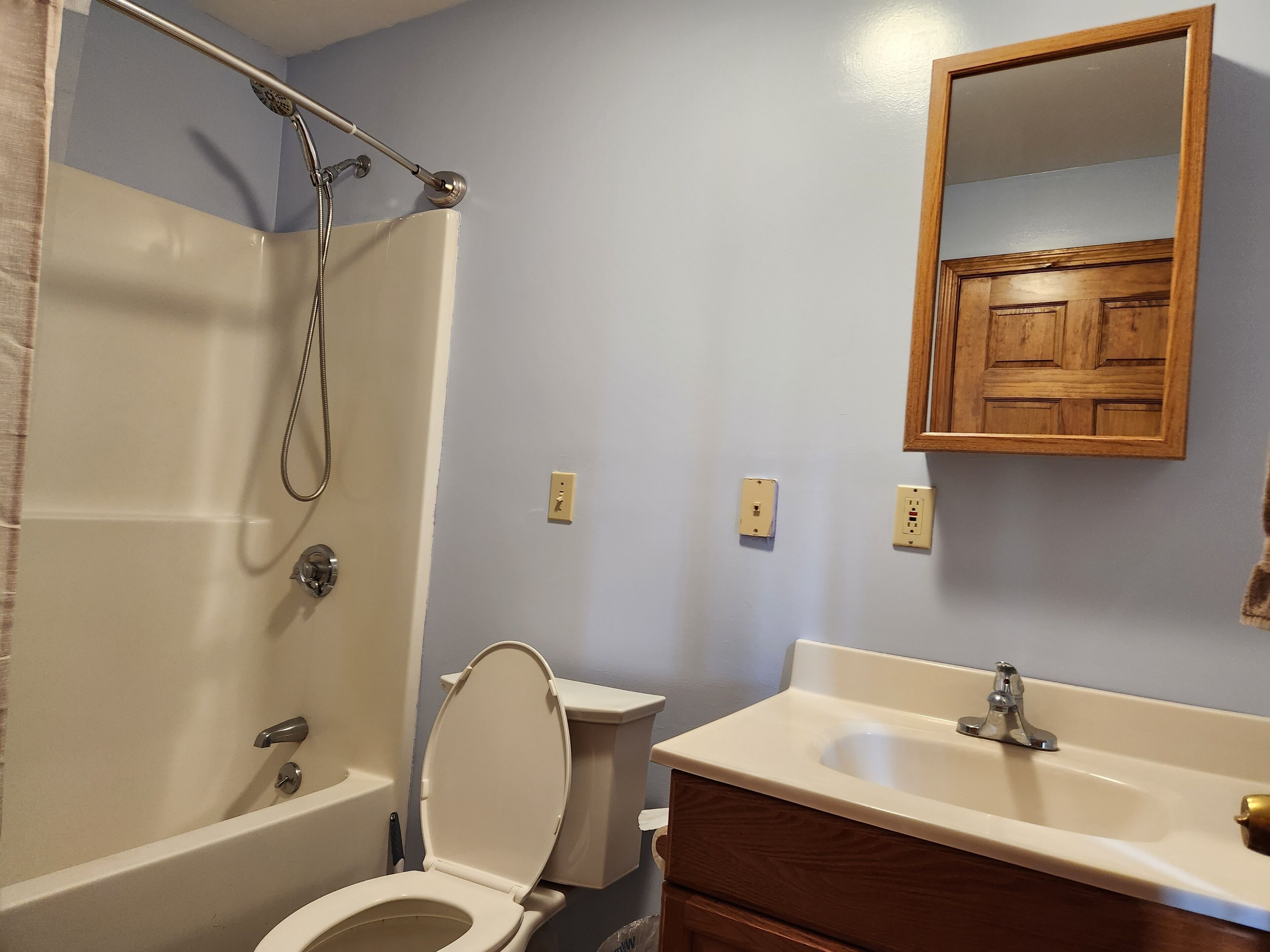 A bathroom with a bathtub, toilet, sink, and a wooden cabinet.