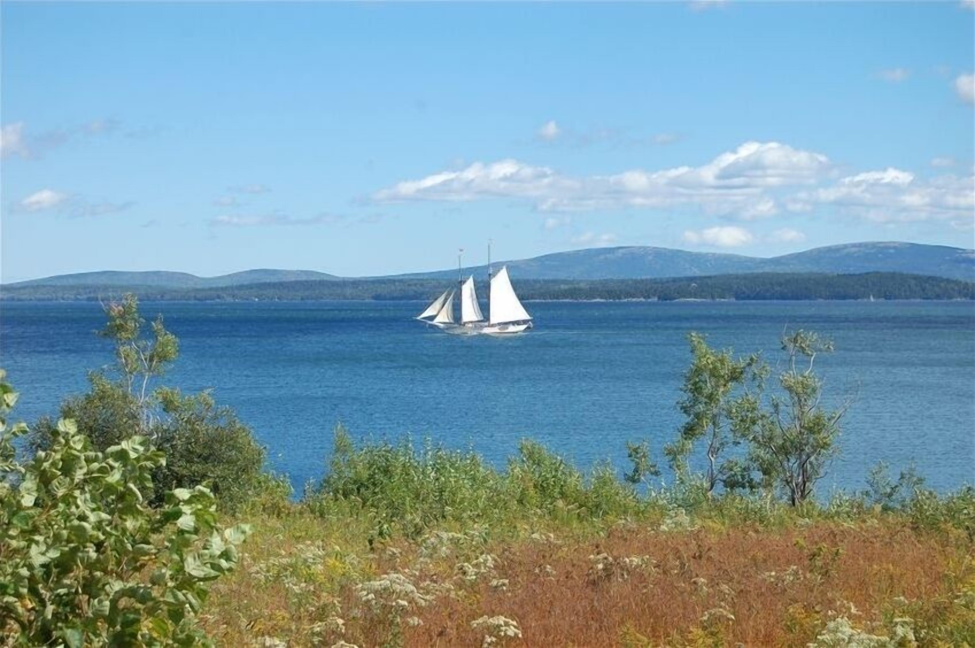 En segelbåt på en stilla sjö med avlägsna berg i bakgrunden.