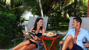 Zwei Personen sitzen draußen auf Liegestühlen, mit einer Fruchtschale und Weingläsern.