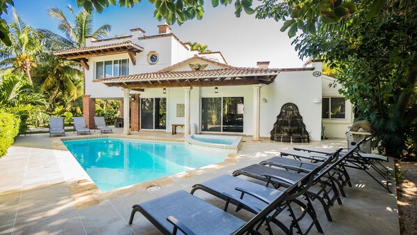 A house with a swimming pool, lounge chairs, and a garden.