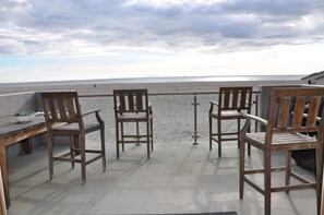 Un balcón con tres sillas de madera y una mesa, con vista a la playa.