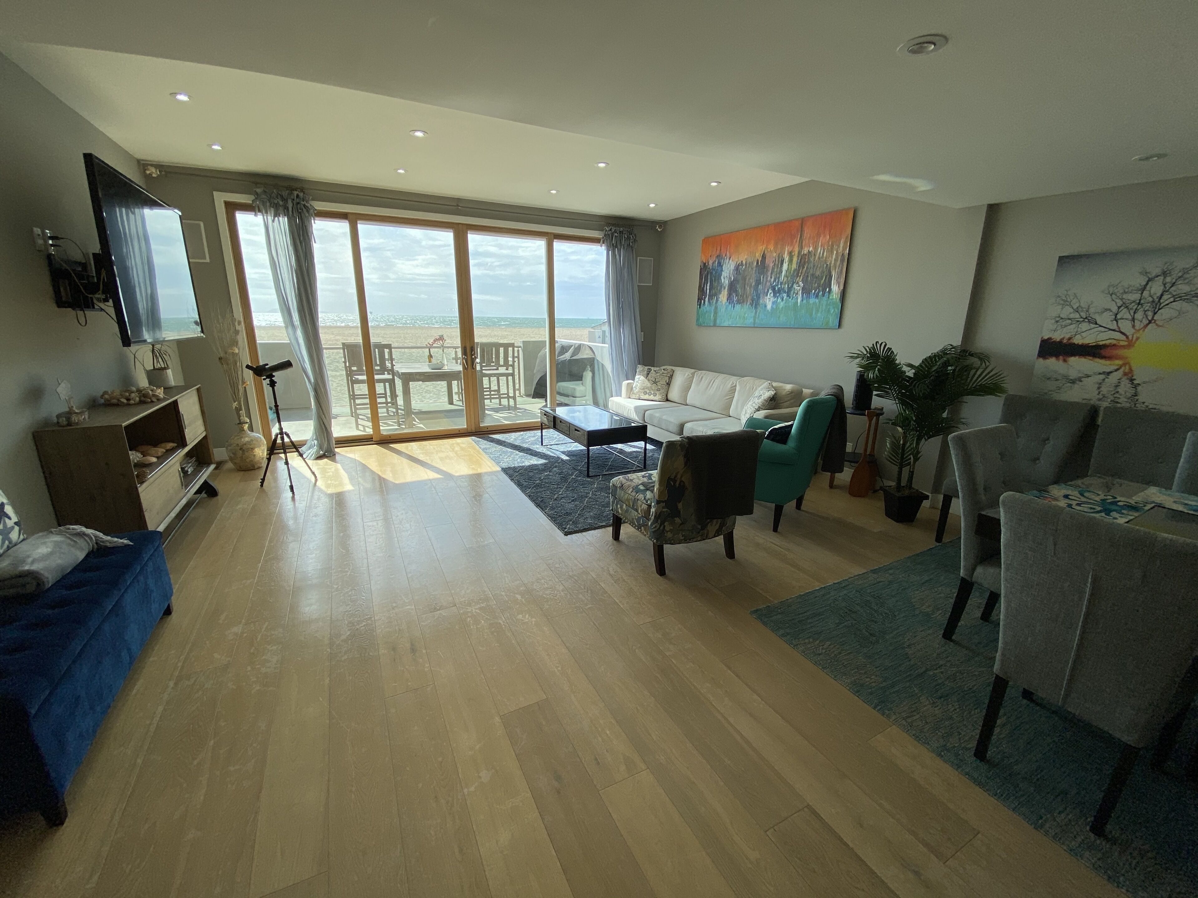A spacious living room with a large sliding glass door leading to a balcony, a sofa, a coffee table, and a TV mounted on the wall.
