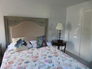 A bed with a colorful quilt, a wooden headboard, and a bedside table with a lamp and a digital clock. - Rustic Quaint Cottage With Spectacular Views (Lottsburg)