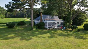 A small, single-story house with a glassed-in porch, surrounded by well-maintained lawns and trees.