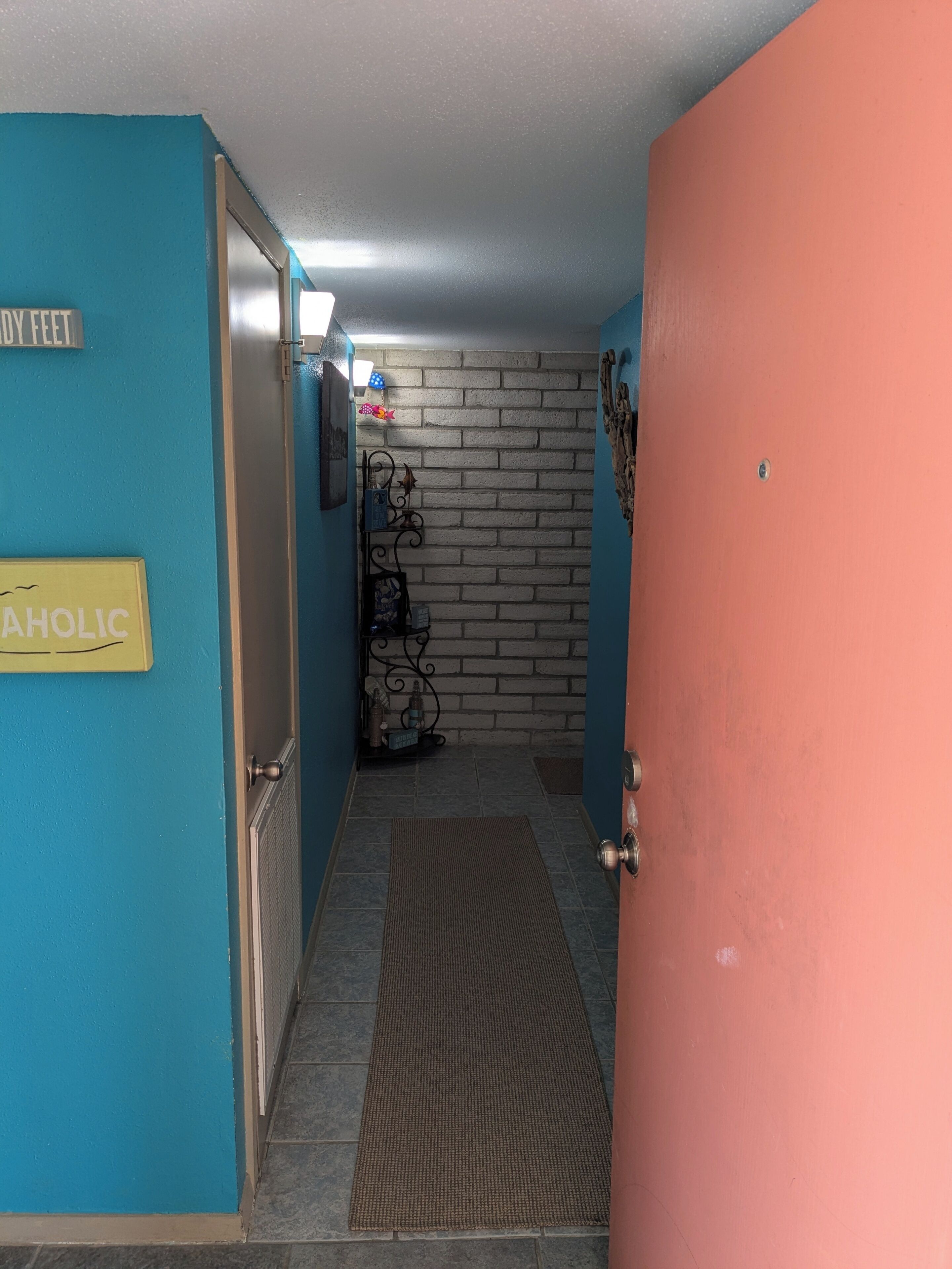 Käytävä, jossa on sininen seinä, keltainen opastekyltti, punainen ovi ja taustalla tiiliseinä.