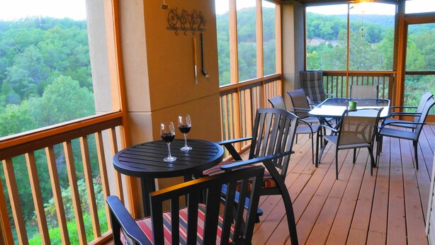 Eine Holzterrasse mit Tisch, Stühlen, zwei Weingläsern und Blick auf ein bewaldetes Gebiet.
