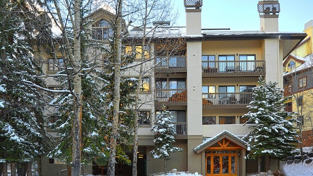 A multi-story hotel with balconies, a snow-covered entrance, and a mountainous backdrop. - Townsend Place 205 | 2BR Ski-In/Ski-Out Condo, Hot Tub (Avon)