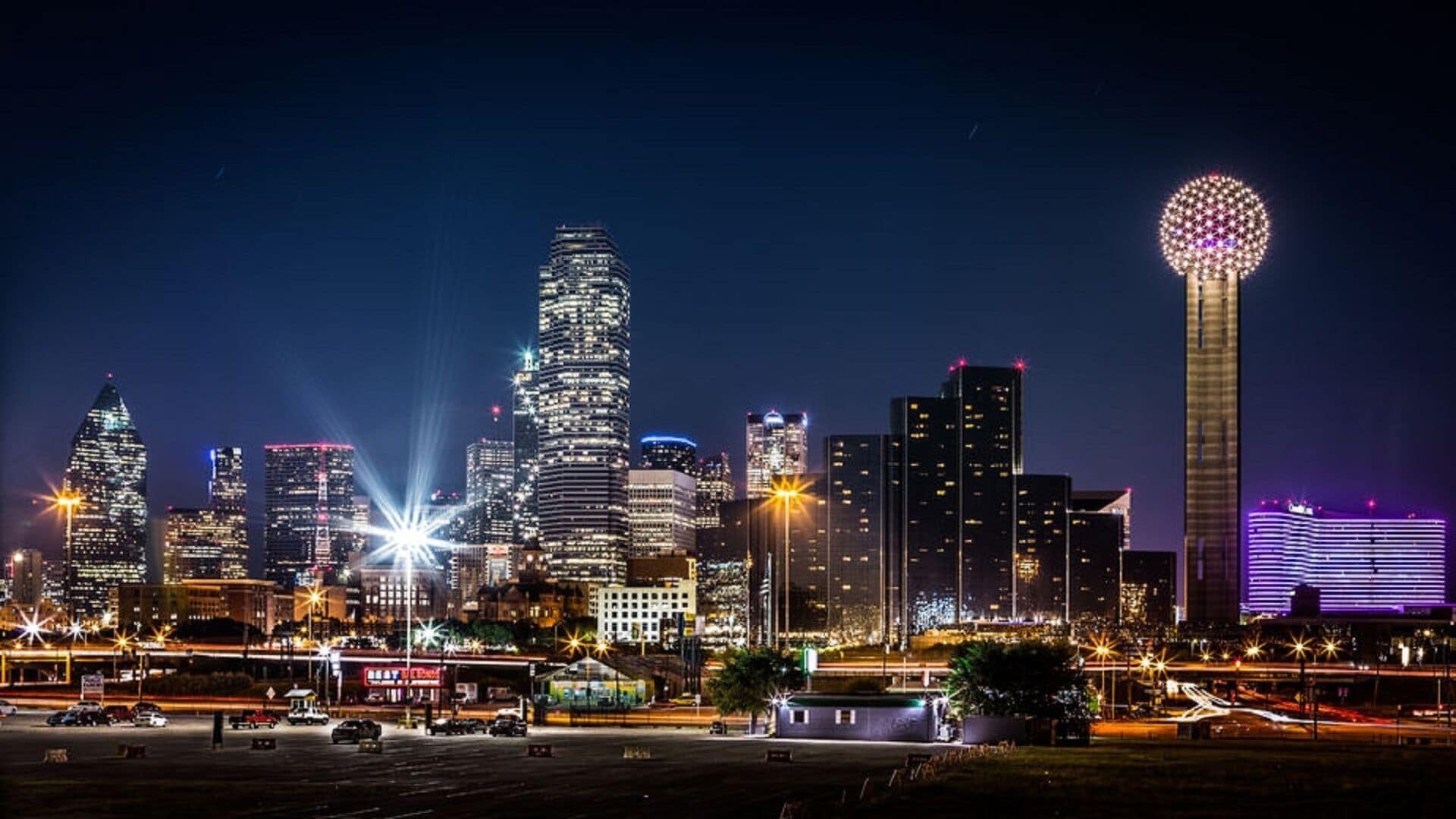 A city skyline at night with illuminated buildings and a prominent tower.