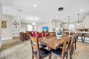 Un comedor amplio con una gran mesa de madera y sillas, una cocina con armarios blancos y una sala de estar con sofás rojos.