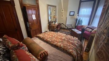 A bedroom with a large bed, a wooden door, a mirror, and a window with curtains.