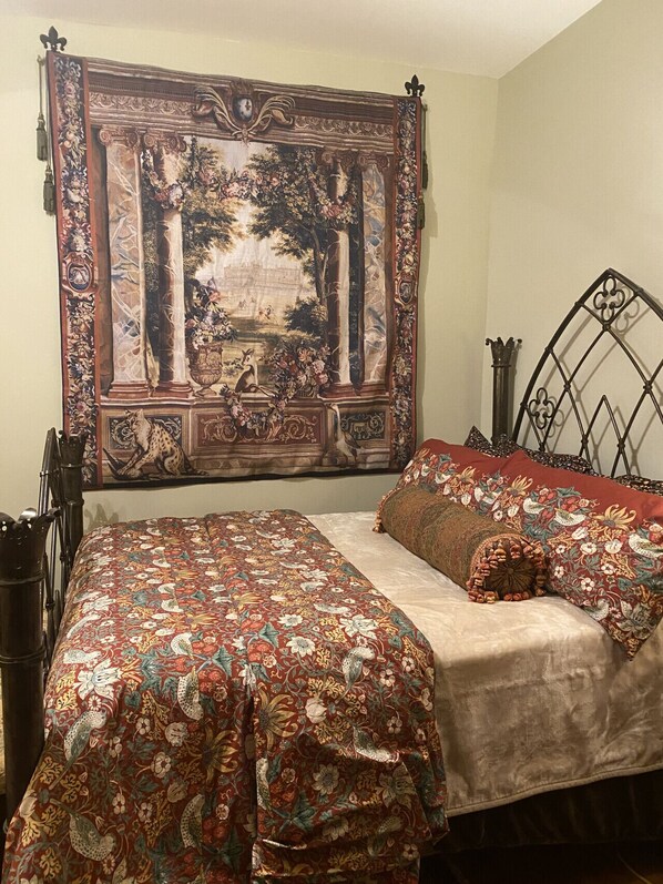 Un dormitorio con un tapiz grande en la pared, una cama con ropa de cama floral y un cabecero de metal.