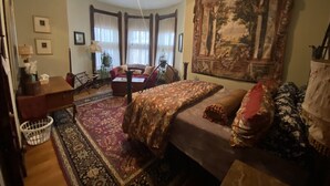 A cozy bedroom with a bed, a desk, a chair, and a large tapestry on the wall.
