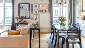 A modern living room with a sofa, dining table, and chairs. There is a large mirror, artwork on the walls, and a view of the outside through large windows. - Wow Eiffel Tower View, Unbelievably Elegant & Spacious (Paris)