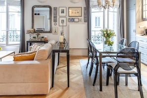 Een moderne woonkamer met een bank, eettafel en stoelen. Er is een grote spiegel, kunst aan de muren en uitzicht op het exterieur door grote ramen.