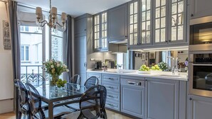 A modern kitchen with grey cabinets, a glass dining table, and a chandelier. - Wow Eiffel Tower View, Unbelievably Elegant & Spacious (Paris)