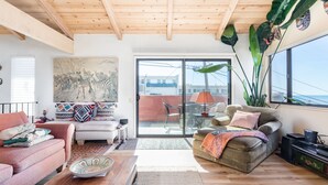 Een ruime woonkamer met een houten plafond, een groot schilderij en een schuifdeur naar een buitenruimte.