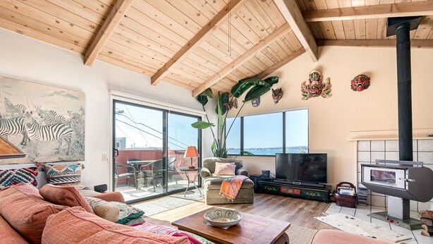 Een ruime woonkamer met een hoge plafond, een groot raam, een televisie, een open haard en een balkon met tuinmeubilair.