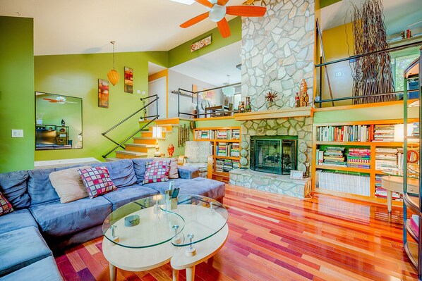 A modern living room with a sectional sofa, a fireplace, a bookshelf, and a staircase leading to an upper level. - Urban Escape w/Hot Tub, Backyard Oasis, Min to Uptown! (Charlotte)