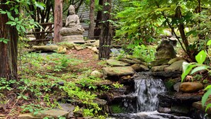 Ein friedlicher Garten mit einem kleinen Wasserfall, Steinfiguren und üppigem Grün.
