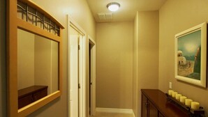 Un corridoio con un armadietto in legno, uno specchio, una porta, una luce a soffitto e un portacandele a parete.