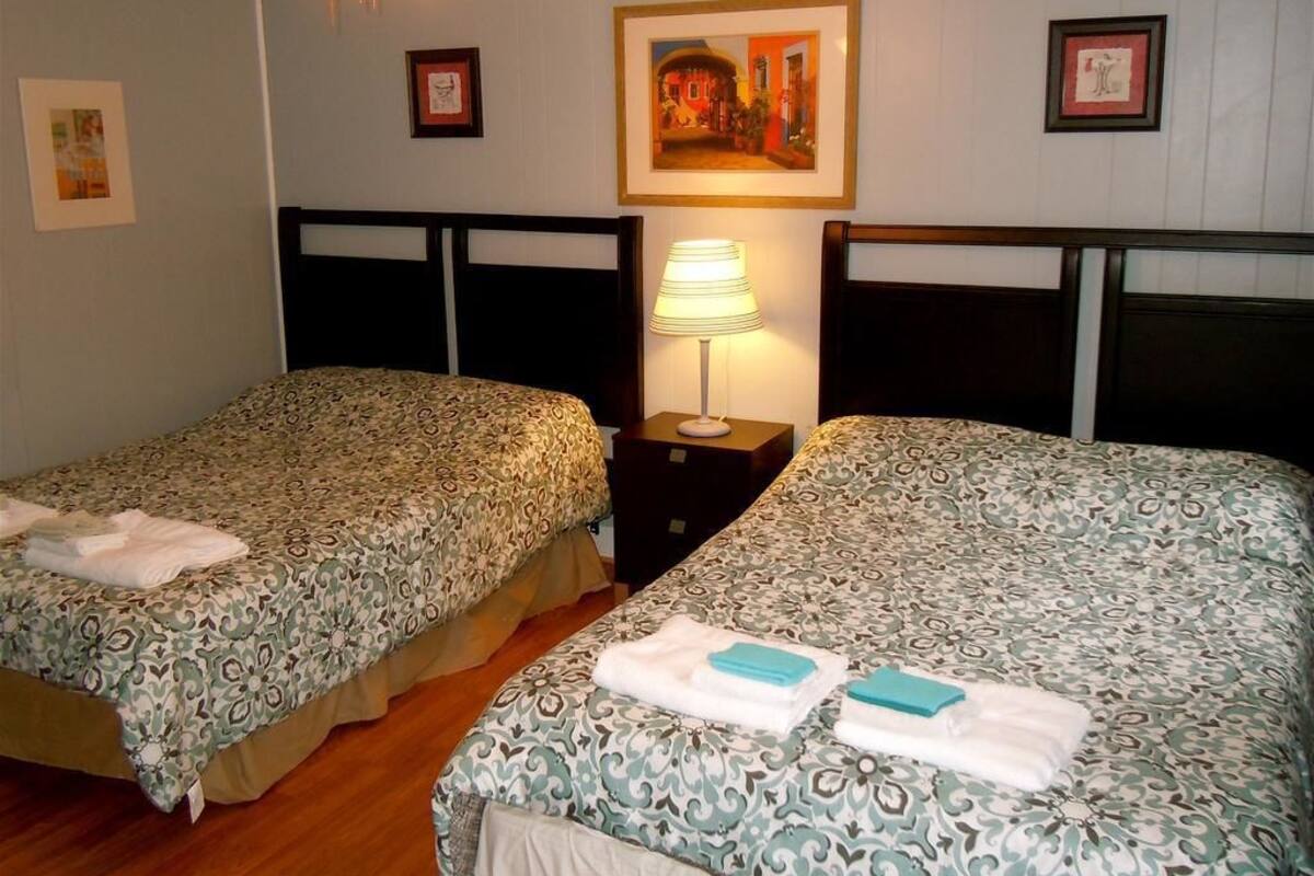 Ein Hotelzimmer mit zwei Einzelbetten, einem Deckenventilator, einer Wandlampe und gerahmten Kunstwerken.