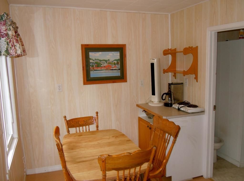 A dining area with a wooden table and chairs, a framed picture on the wall, and a coffee maker on a counter.