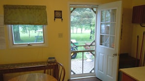 Una habitación con una mesa de madera, un banco, una puerta que da al exterior y una ventana pequeña con cortina.