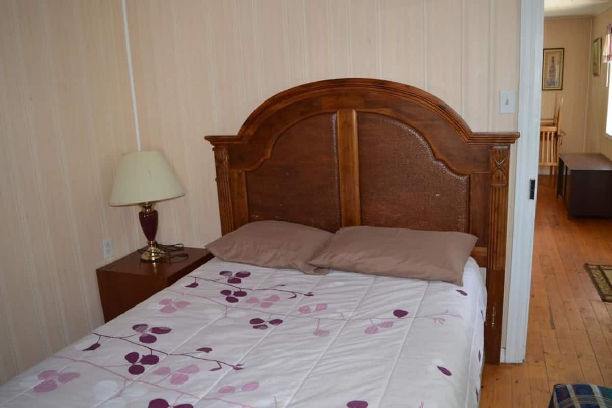 Ein Schlafzimmer mit einem hölzernen Kopfteil, einem Bett mit blumigem Überwurf, einer Nachttischlampe und einem Nachttisch aus Holz.