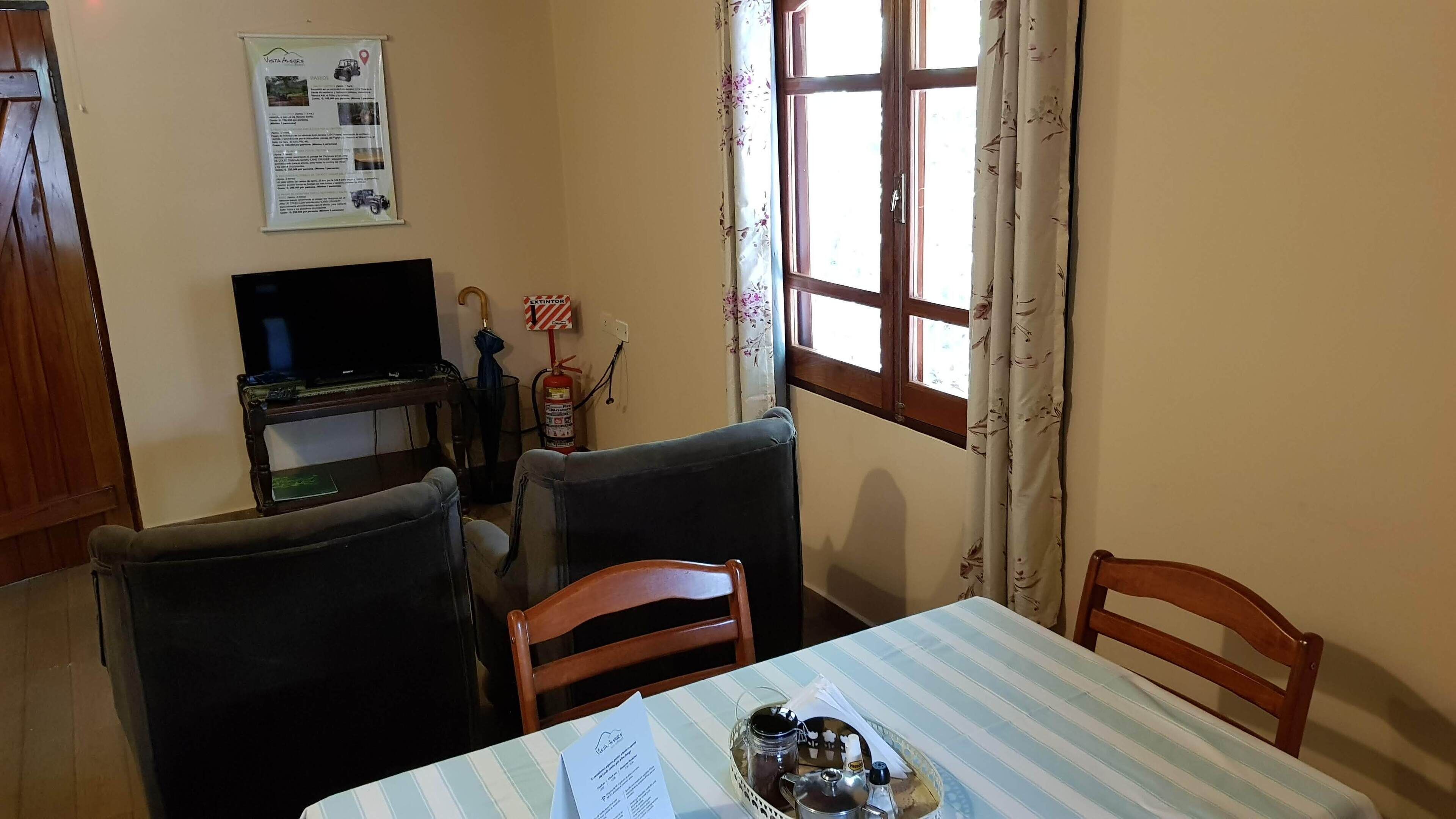 Un coin repas avec une table dressée pour deux personnes, un téléviseur et un extincteur.