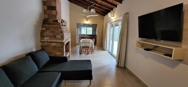 Una sala de estar con sofá, televisor montado en la pared, chimenea y cocina al fondo.
