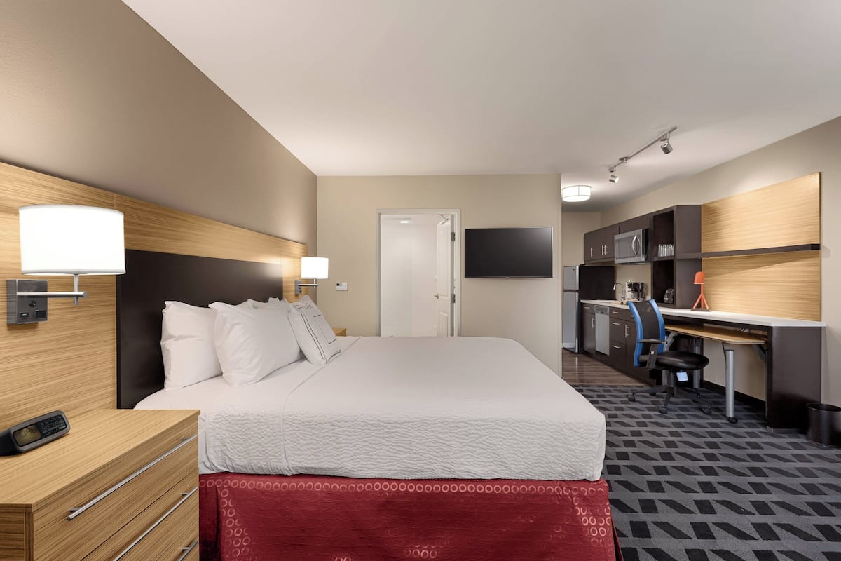 A hotel room with a bed, bedside table, desk, chair, and a TV.