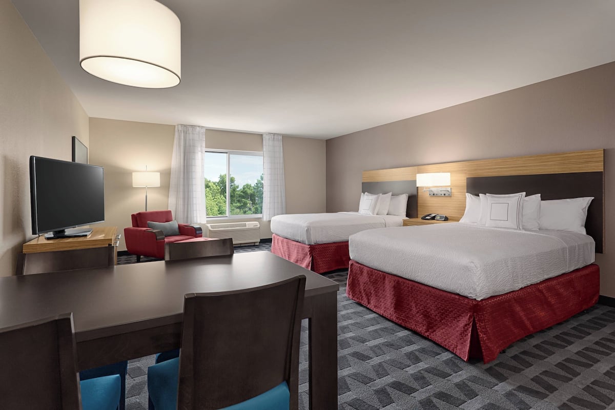 A hotel room with two beds, a desk, a TV, and a view of the outdoors.