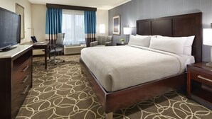 Ein Hotelzimmer mit einem großen Bett, einem Schreibtisch mit Stuhl, einem Fernseher und einem Fenster mit Vorhängen.