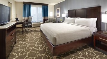 Una habitación de hotel con una cama grande, un escritorio con una silla, un televisor y una ventana con cortinas.