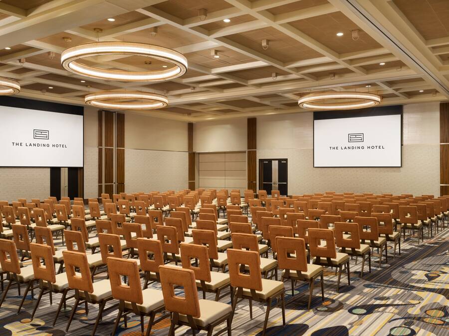 Un salón de conferencias con filas de sillas y una pantalla grande mostrando el logotipo de The Landing Hotel.