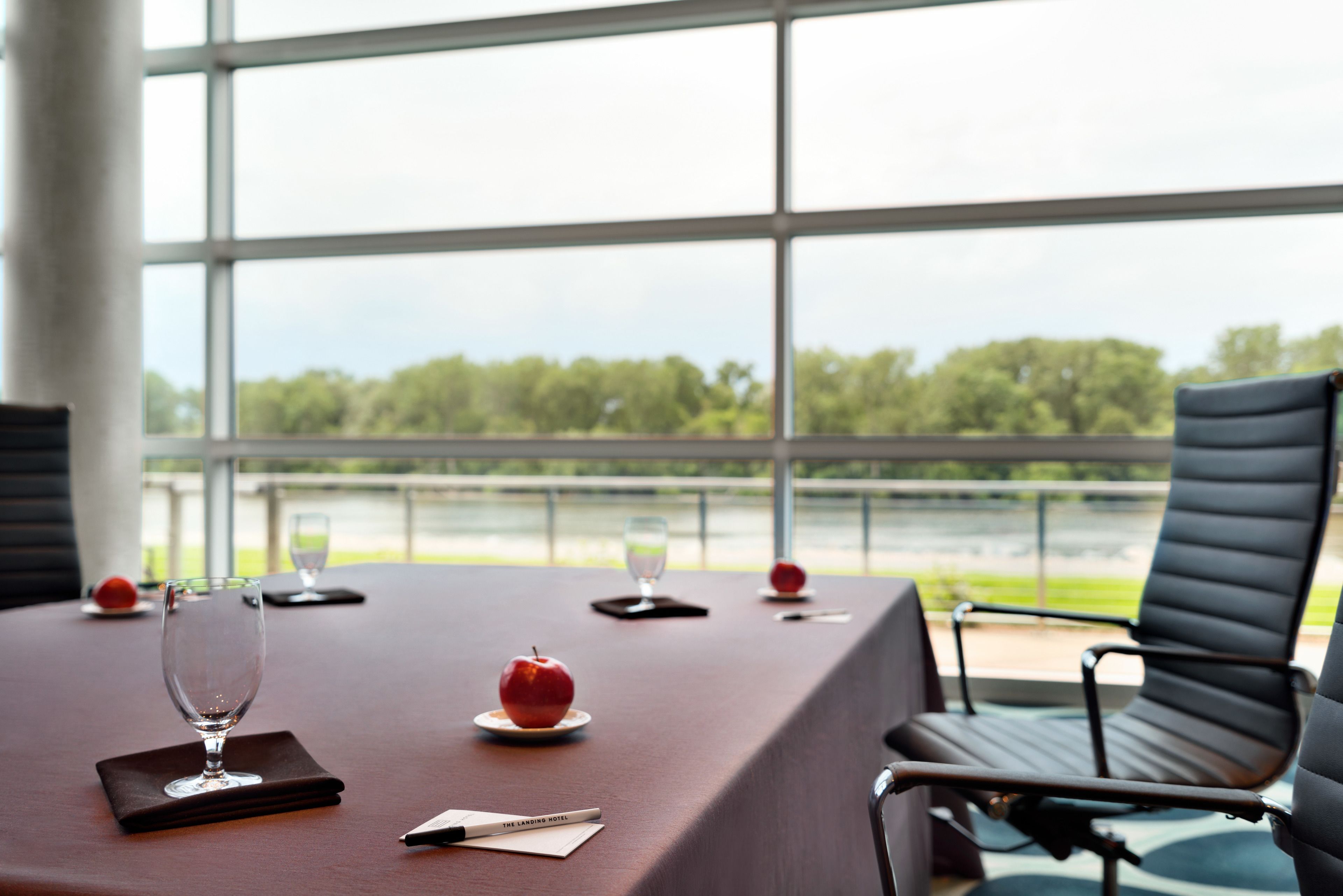 Ein Konferenztisch mit Blick auf einen Fluss und Bäume durch große Fenster.