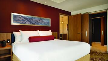 A large bed with white and red bedding, a wooden headboard, a nightstand with a phone, and a painting on the wall.