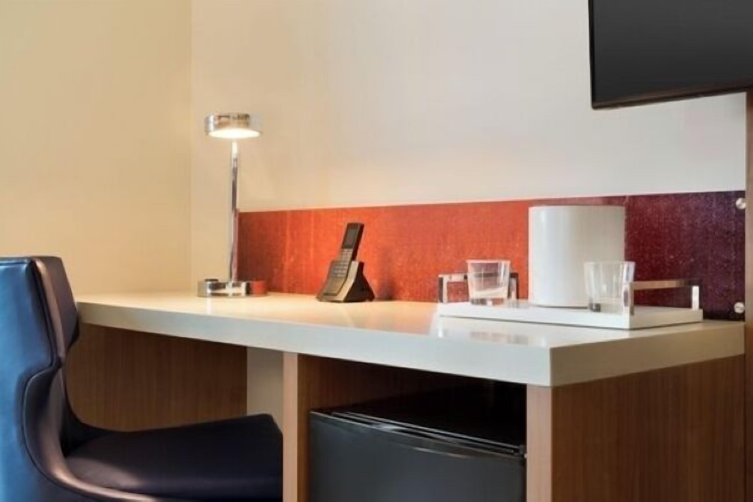 Una mesa de recepción de hotel con un teléfono, una lámpara y una cafetera.