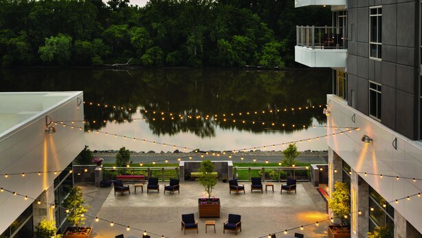 A rooftop patio with outdoor seating, a view of a lake, and string lights. - The Landing Hotel at Rivers Casino Schenectady (Schenectady)