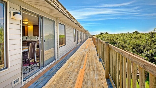 Eine Holzterrasse mit Geländer, die zu einem Gebäude mit großen Fenstern und einer Tür führt.