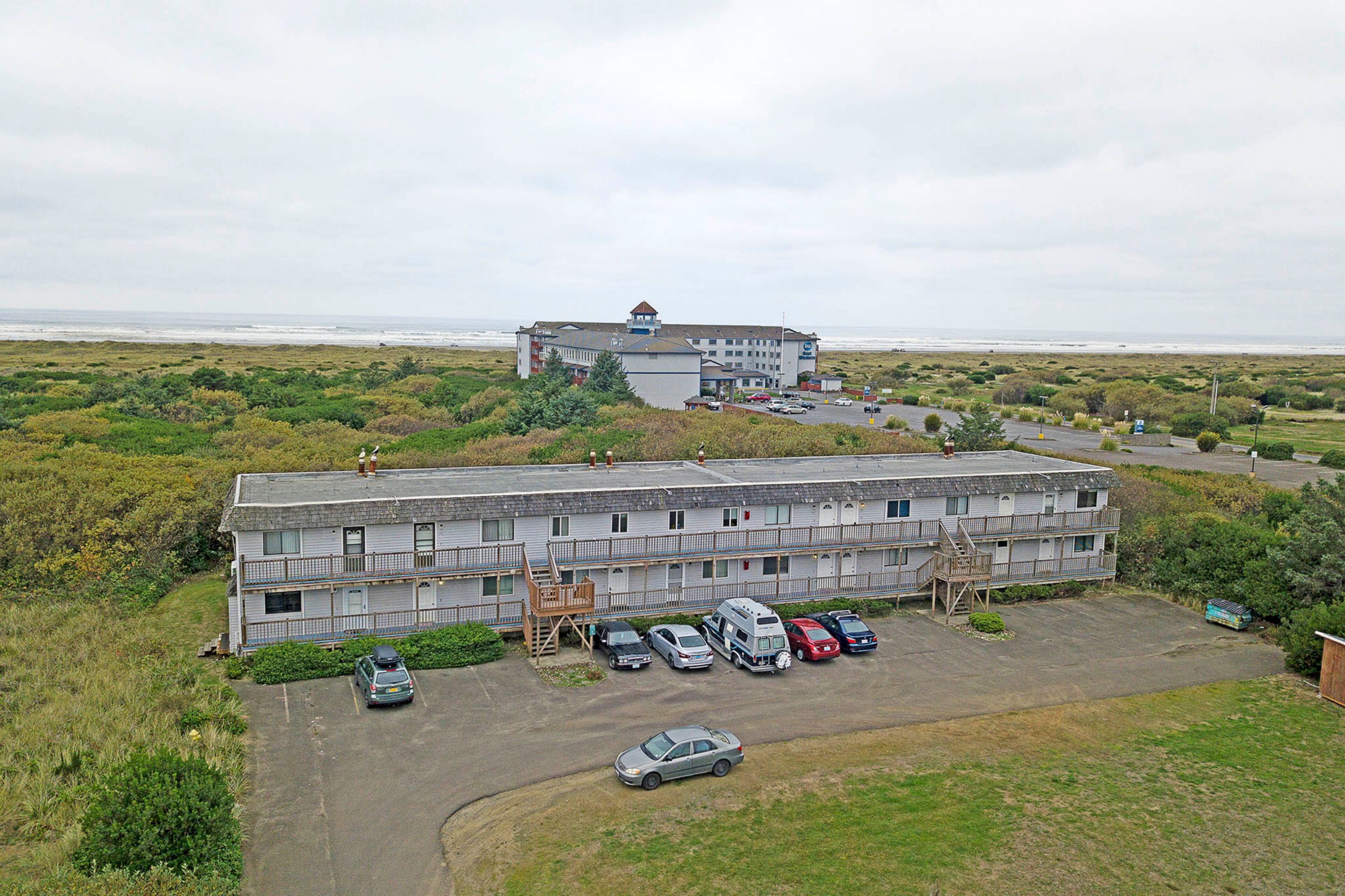 A motel with a parking lot, a small building with a balcony, and a view of the ocean.