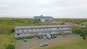 A motel with a parking lot, a small building with a balcony, and a view of the ocean.