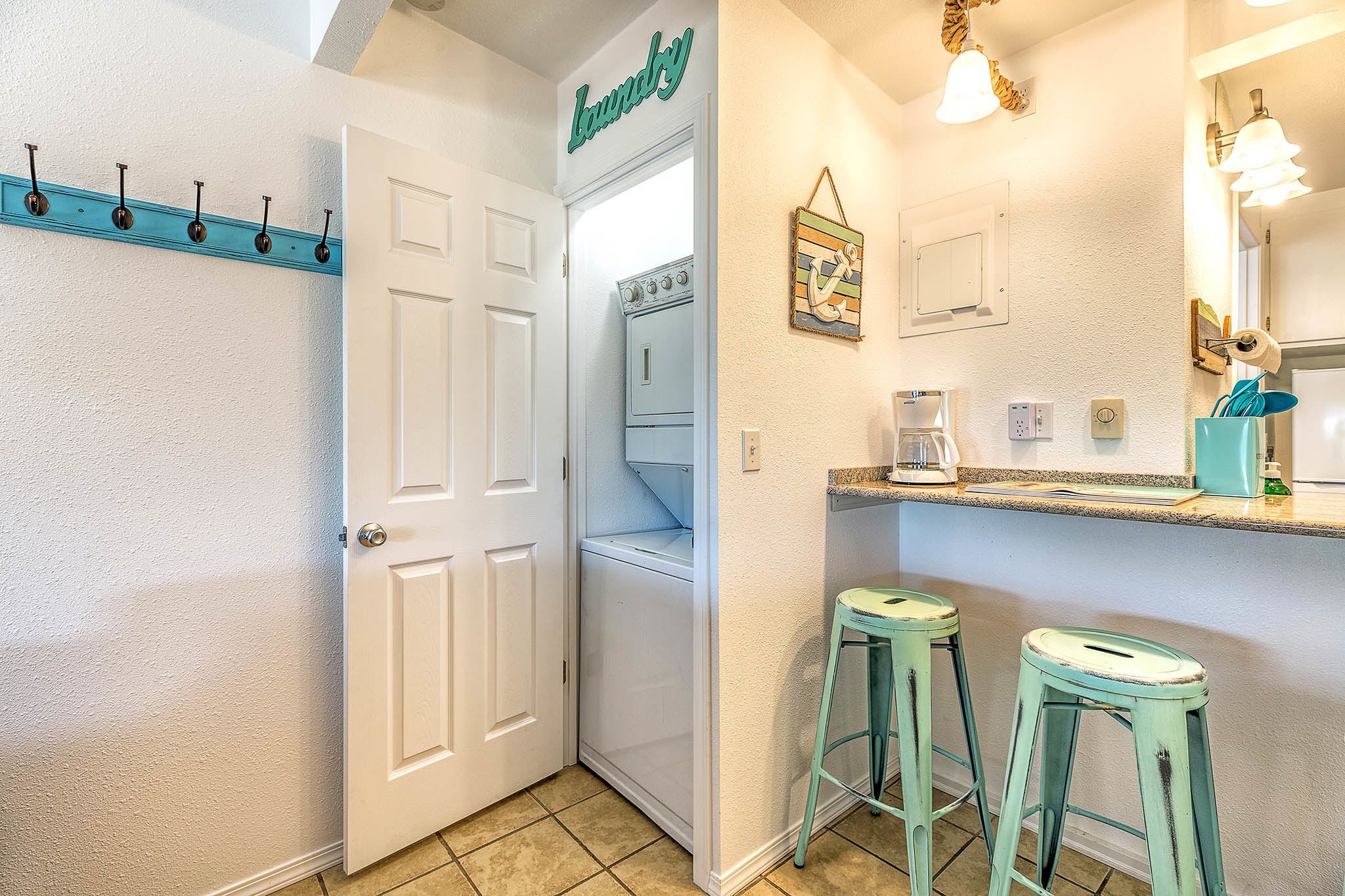 A laundry room with a white door, a wall-mounted laundry sign, a white dryer, and two green stools.
