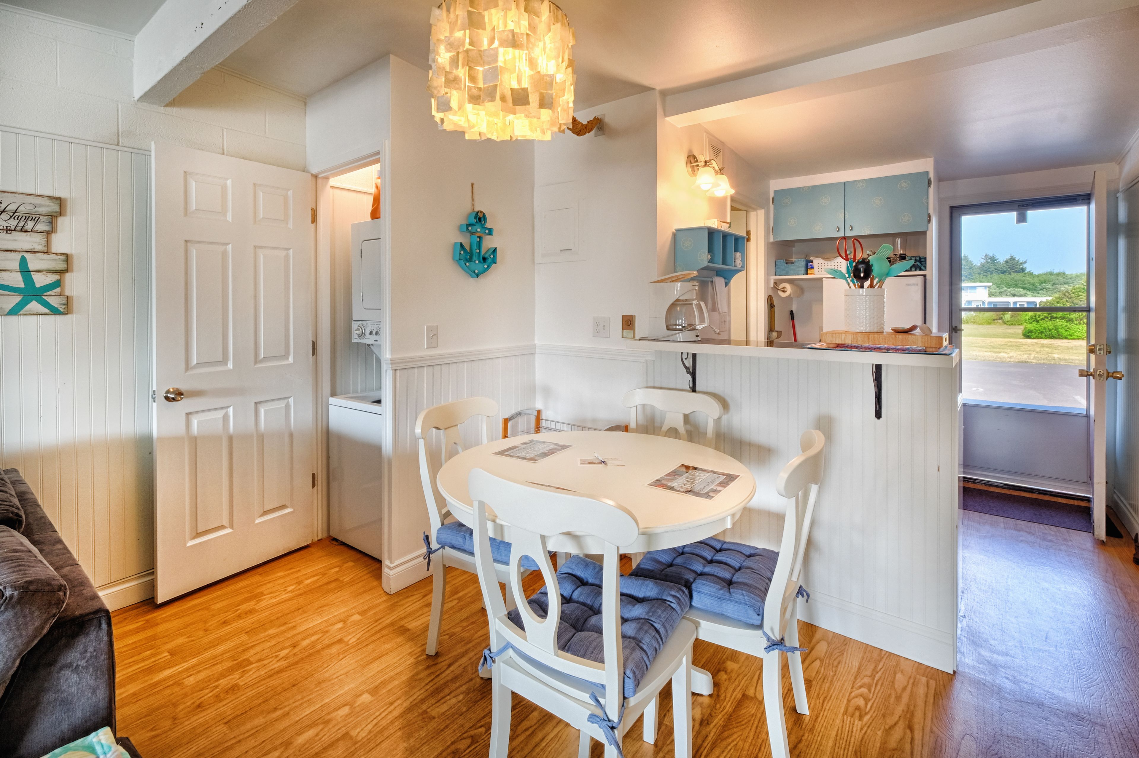 A cozy kitchen with white cabinetry, a round dining table with blue cushioned chairs, and a hanging light fixture.
