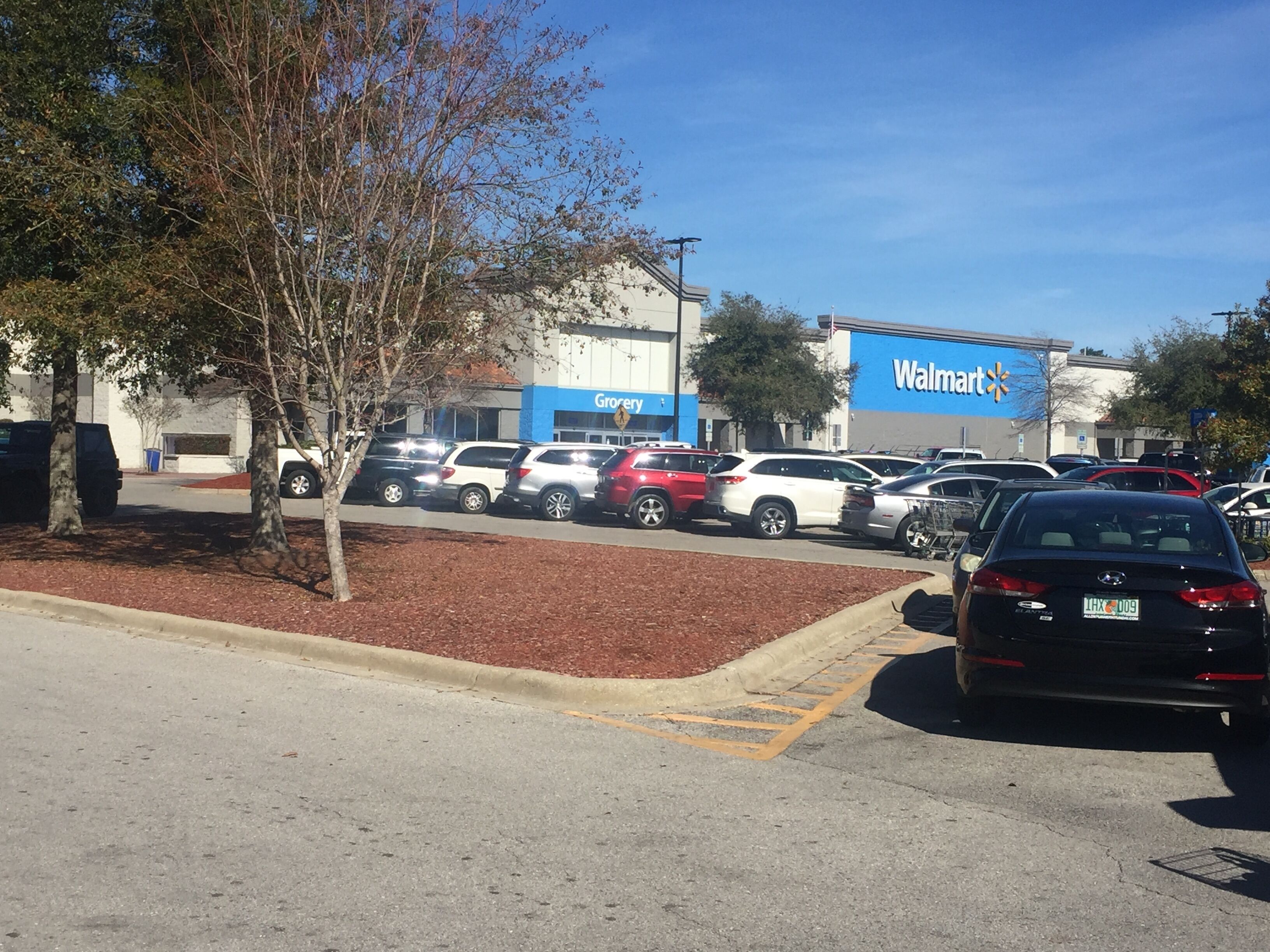 Un pàrquing amb diversos cotxes i un Walmart al fons.