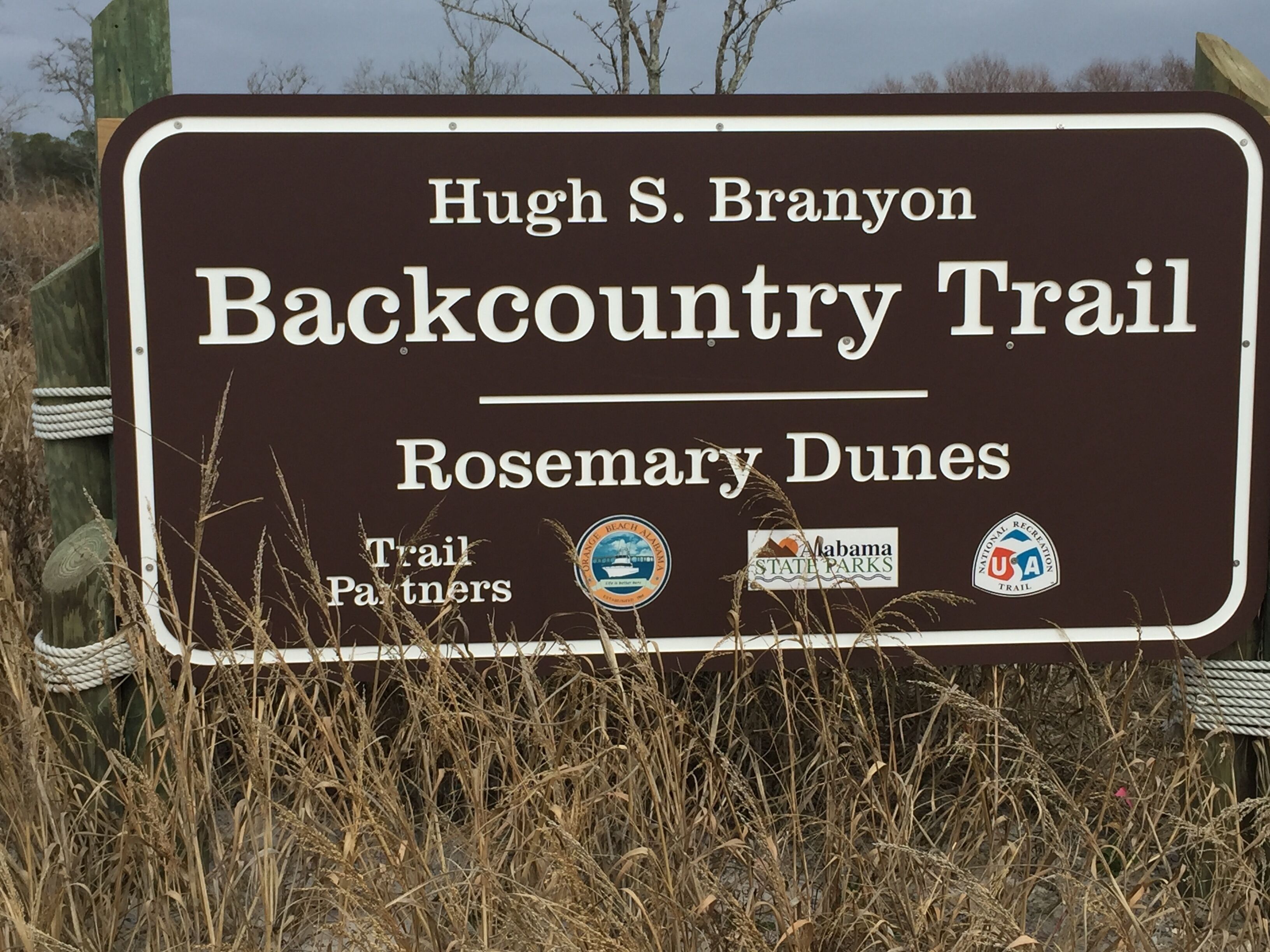 A sign for the Hugh S. Branyon Backcountry Trail in Rosemary Dunes, featuring logos of trail partners.