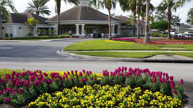 Un hotel con entrada cubierta, palmeras y un jardín ajardinado con flores.